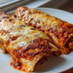 Two baked High Protein Chicken Enchiladas smothered in red sauce and melted white cheese on a white plate.