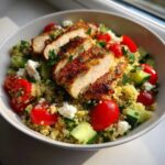Close-up of a quinoa salad topped with sliced grilled chicken, cherry tomatoes, cucumber, and feta cheese, perfect for Easy Summer Meals.