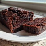 Close-up of a very moist chocolate zucchini bread loaf, partially sliced, showing its rich, dark crumb.