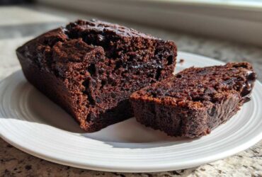 Close-up of a very moist chocolate zucchini bread loaf, partially sliced, showing its rich, dark crumb.