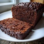 A close-up of a slice cut from a very Moist Chocolate Zucchini Bread loaf topped with chocolate chips.