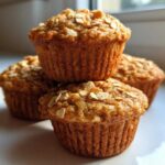 A close-up stack of three golden brown, oatmeal-topped Peanut Free Breakfast Muffins.