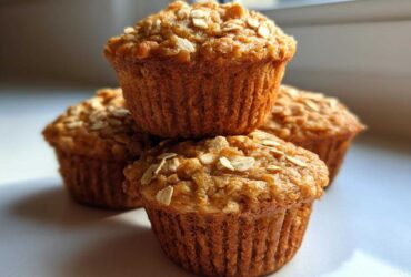 A close-up stack of three golden brown, oatmeal-topped Peanut Free Breakfast Muffins.