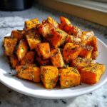 Close-up of perfectly roasted Garlic Parmesan Sweet Potatoes cubes seasoned with herbs on a white plate.