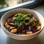 A hearty bowl of Warm Vegan Stew with White Beans and Mushrooms, topped with fresh parsley.