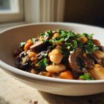 A close-up of a bowl of Warm Vegan Stew with White Beans and Mushrooms, topped with fresh parsley.